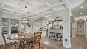 A spacious kitchen with a central island, white cabinetry, and a dining area with a large wooden table and chairs. - Red Rock Farmhouse! Hot Tub, Fire Pit & Trails (Colorado Springs)
