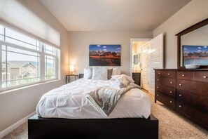Un dormitorio con una cama grande, un aparador y una ventana con vistas a casas.