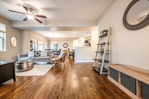 A spacious living room with hardwood flooring, a ceiling fan, a sofa, a coffee table, and a bookshelf. - Pioneer Retreat! Downtown High-End Haven (Colorado Springs)