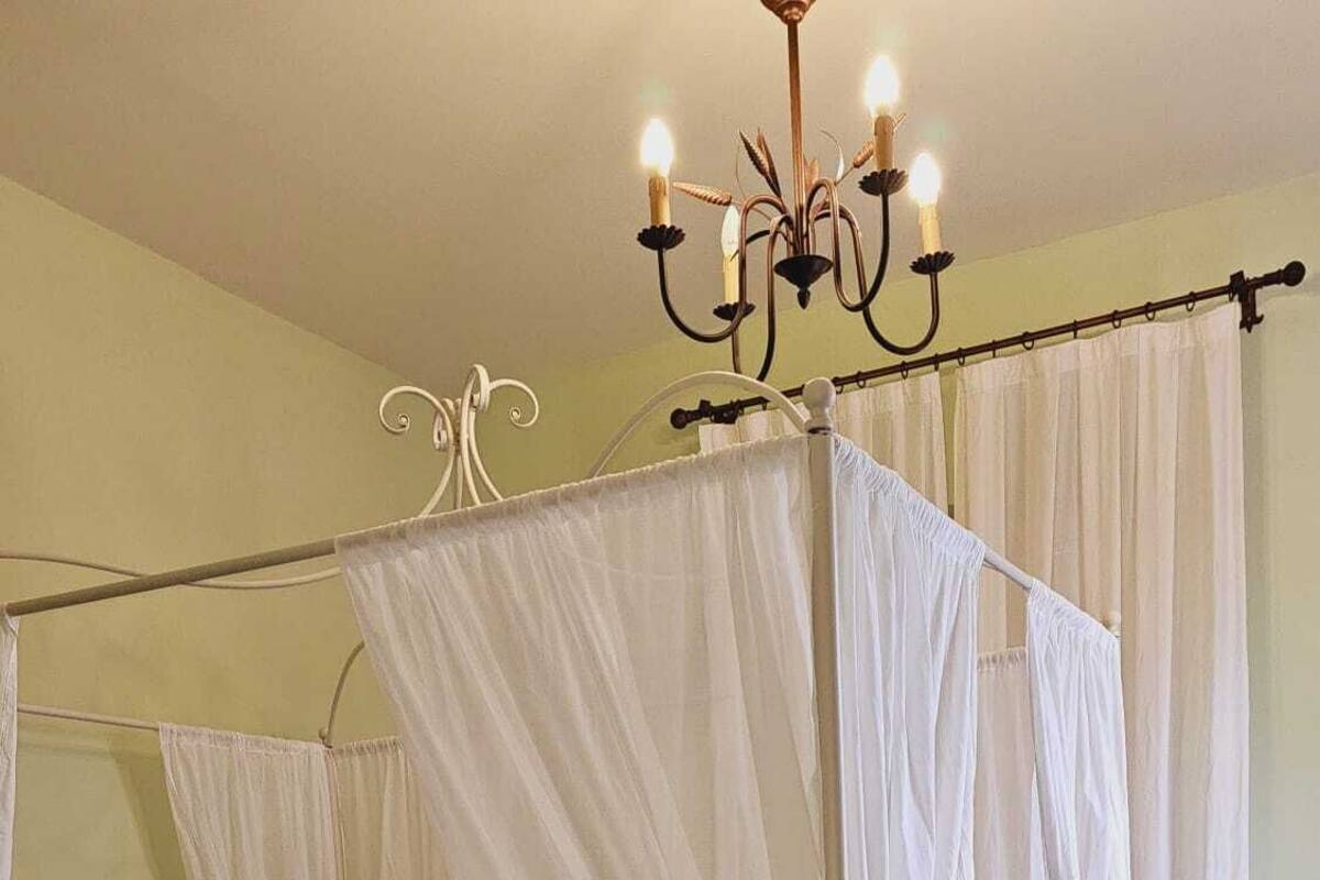 A four-poster canopy bed with a white bedspread and decorative pillows, a metal bed frame, and a woven rug on the floor.
