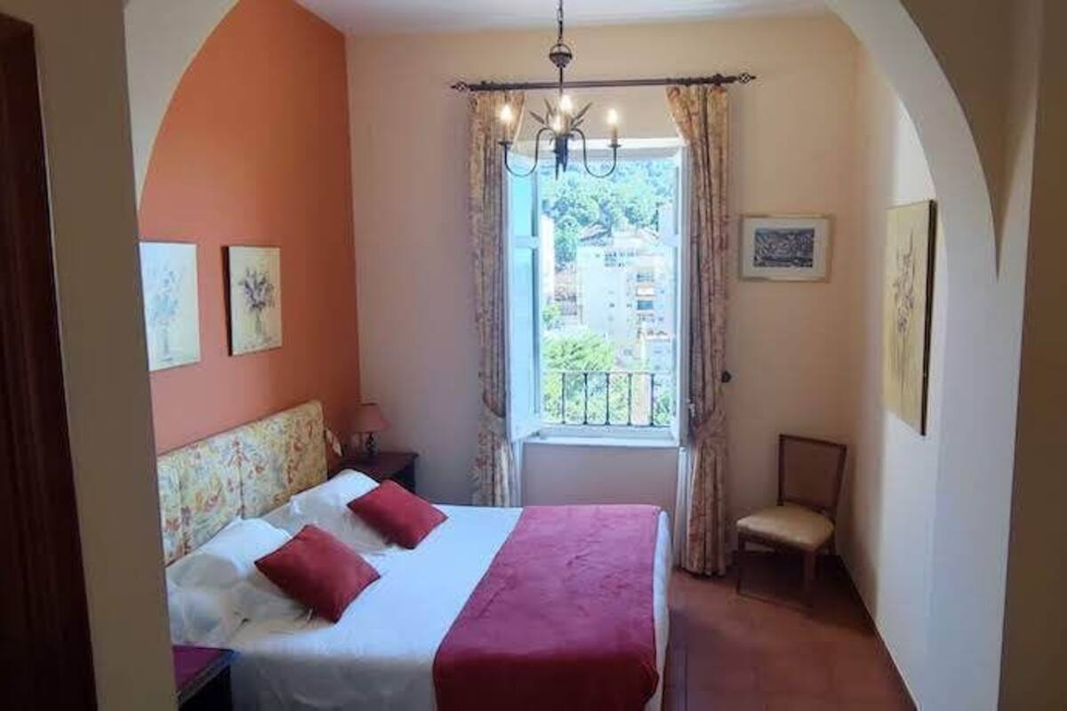 A bedroom with a bed, a chair, a desk, and a window with curtains.