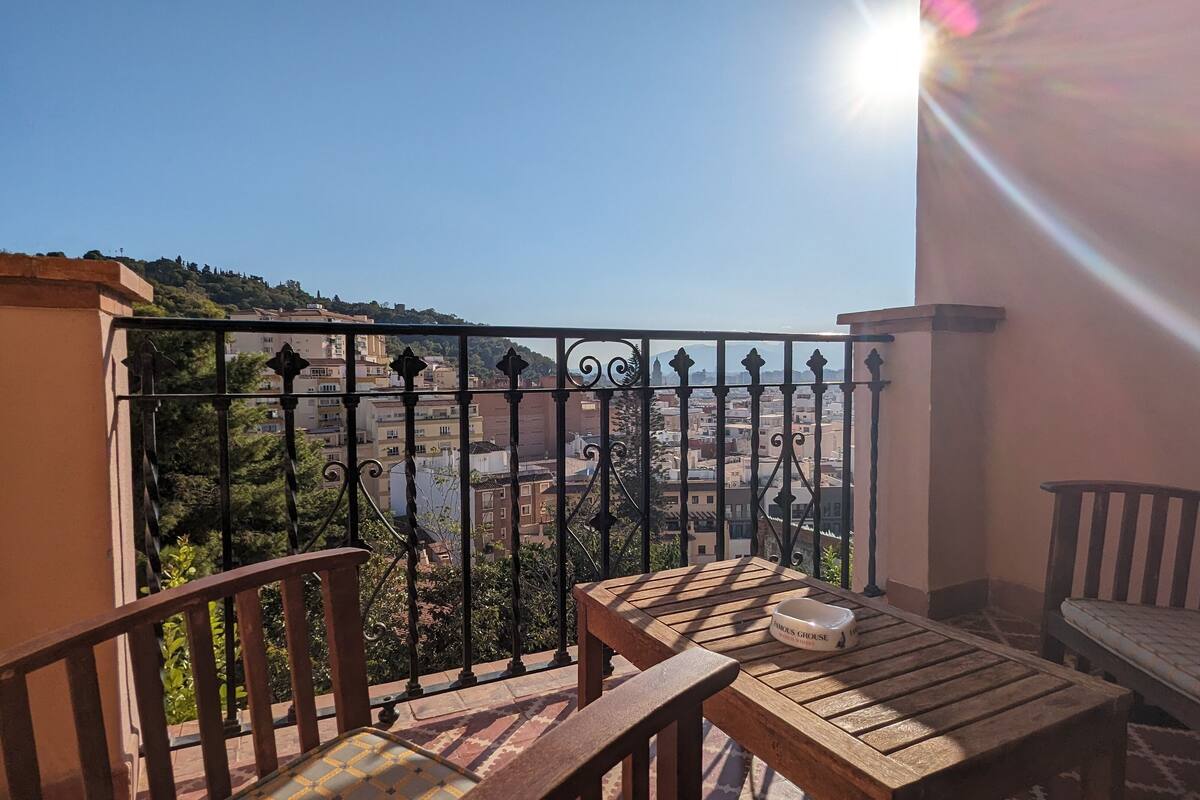 A balcony with a table and chairs, a metal railing, and a view of a cityscape.