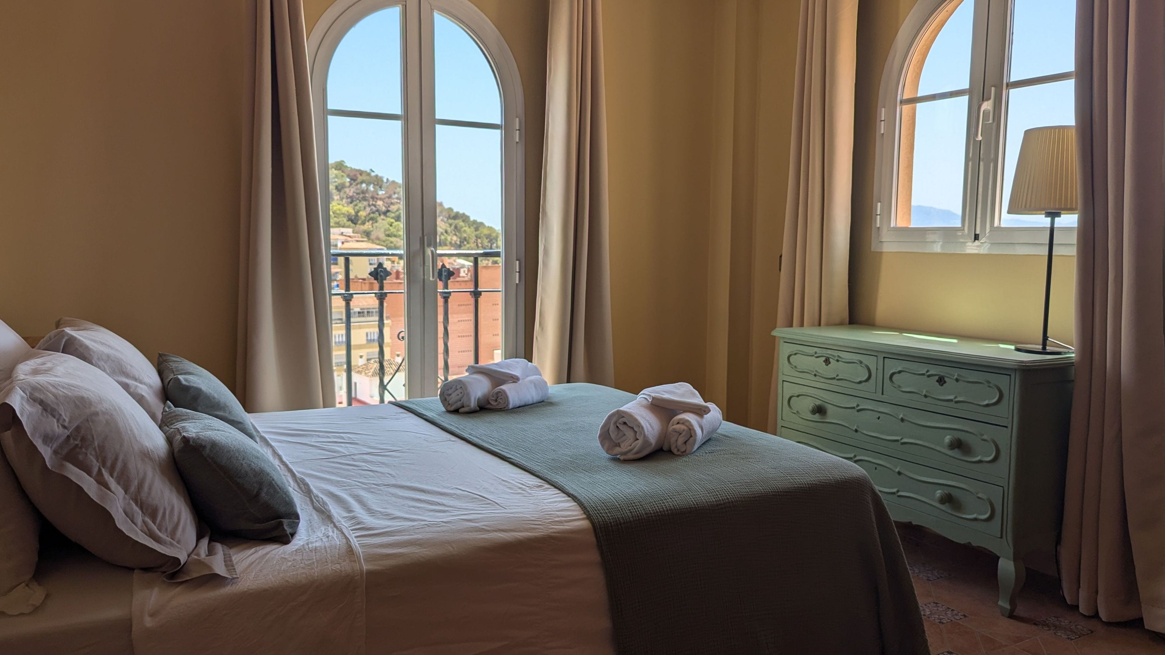 Habitación de hotel con cama, cómoda y vista a un balcón con barandilla.