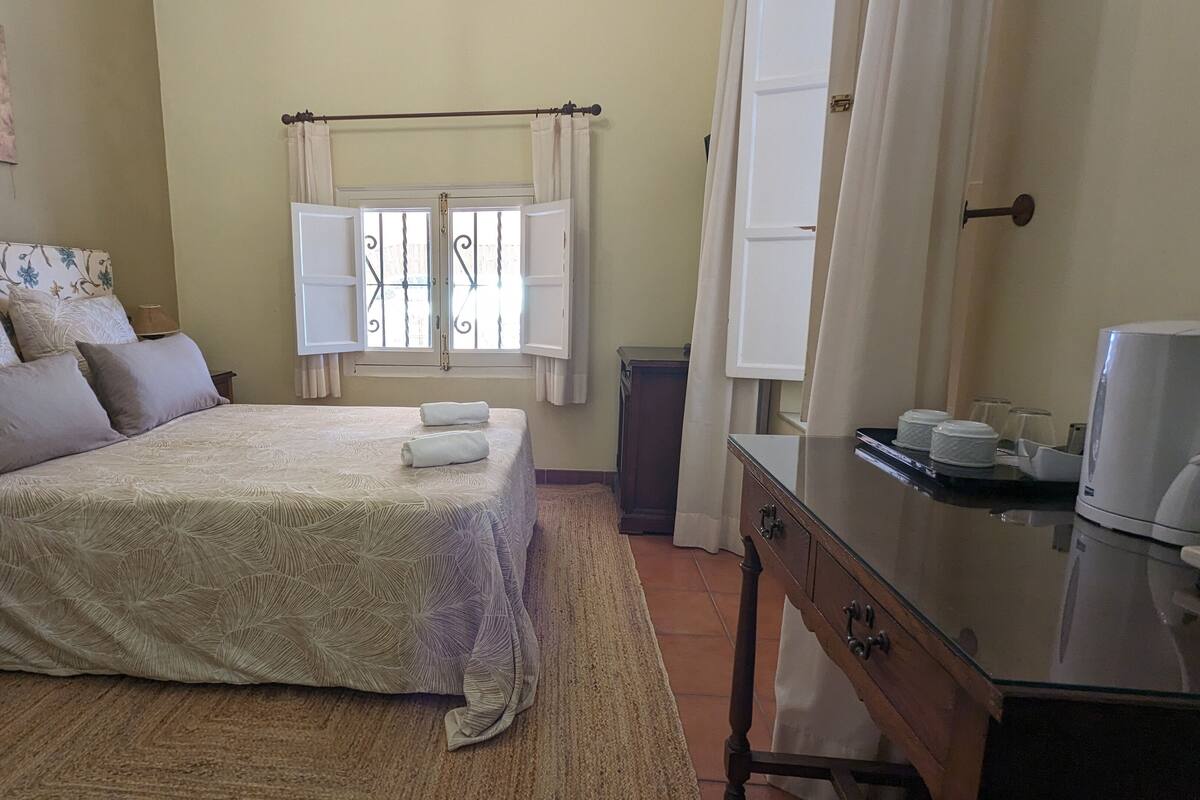 A neatly arranged bedroom with a bed, a bedside table, a dresser, and a window with curtains.
