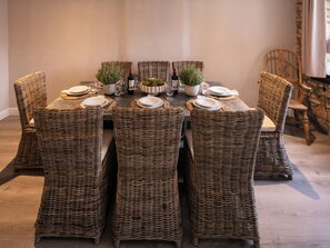 Una mesa de comedor dispuesta con sillas de mimbre, platos, copas y una botella de vino.