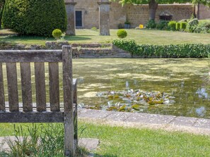 Een houten bank in een tuin met een vijver en stenen muren.