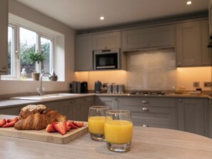 Une cuisine avec un plan de travail en bois, deux verres de jus d’orange et un croissant aux fraises.