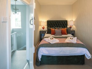 A bedroom with a large bed, two bedside tables with lamps, a headboard, and a view of a hallway.