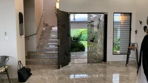 A modern interior with a staircase leading to a garden, a glass door with a leaf pattern, and a metal railing. - Casa Hacienda Jaguar (Ciudad Cortés)