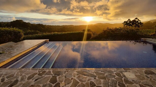 A stone-tiled infinity pool with a clear view of the sunset over a hilly landscape. - Casa Hacienda Jaguar (Ciudad Cortés)