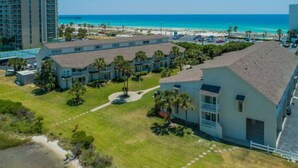 A beachfront hotel with multiple-story buildings, a parking area, and a clear view of the ocean. - Sand Dollar W212 Bayfront Escape- Gorgeous Sunset Views, Bikes Included! (Pensacola Beach)