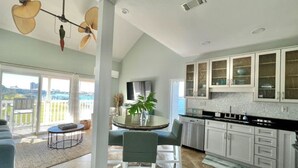 A modern kitchen with white cabinets and a dining area with a round table and chairs. - Sand Dollar W212 Bayfront Escape- Gorgeous Sunset Views, Bikes Included! (Pensacola Beach)