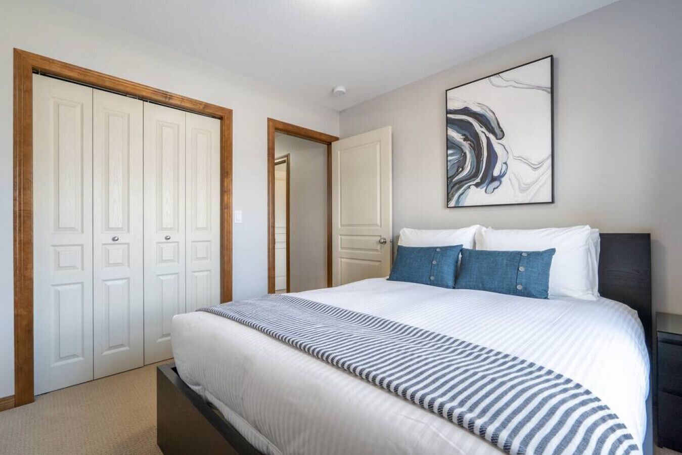 Un dormitori amb llit, una nitòria, un quadre i un armari.