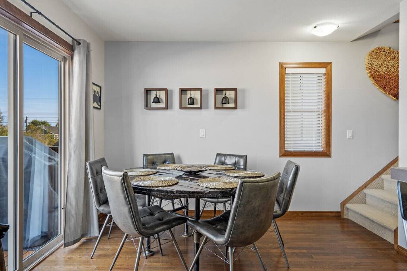 A dining area with a round table, six chairs, and a large window with blinds.