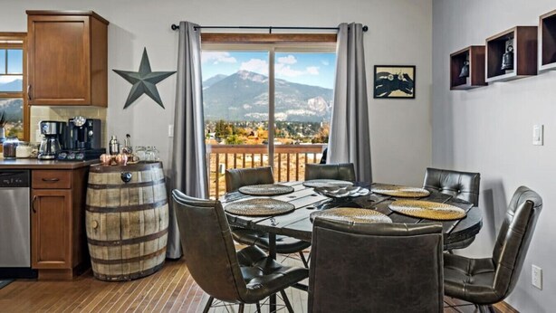 A dining area with a view of mountains, a star decoration, and a kitchen with a coffee maker. - Downtown Basecamp | Stylish | Games Room (Invermere)