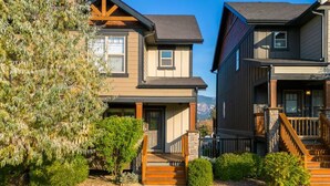A two-story residential building with a front porch, a staircase, and a well-maintained lawn. - Downtown Basecamp | Stylish | Games Room (Invermere)