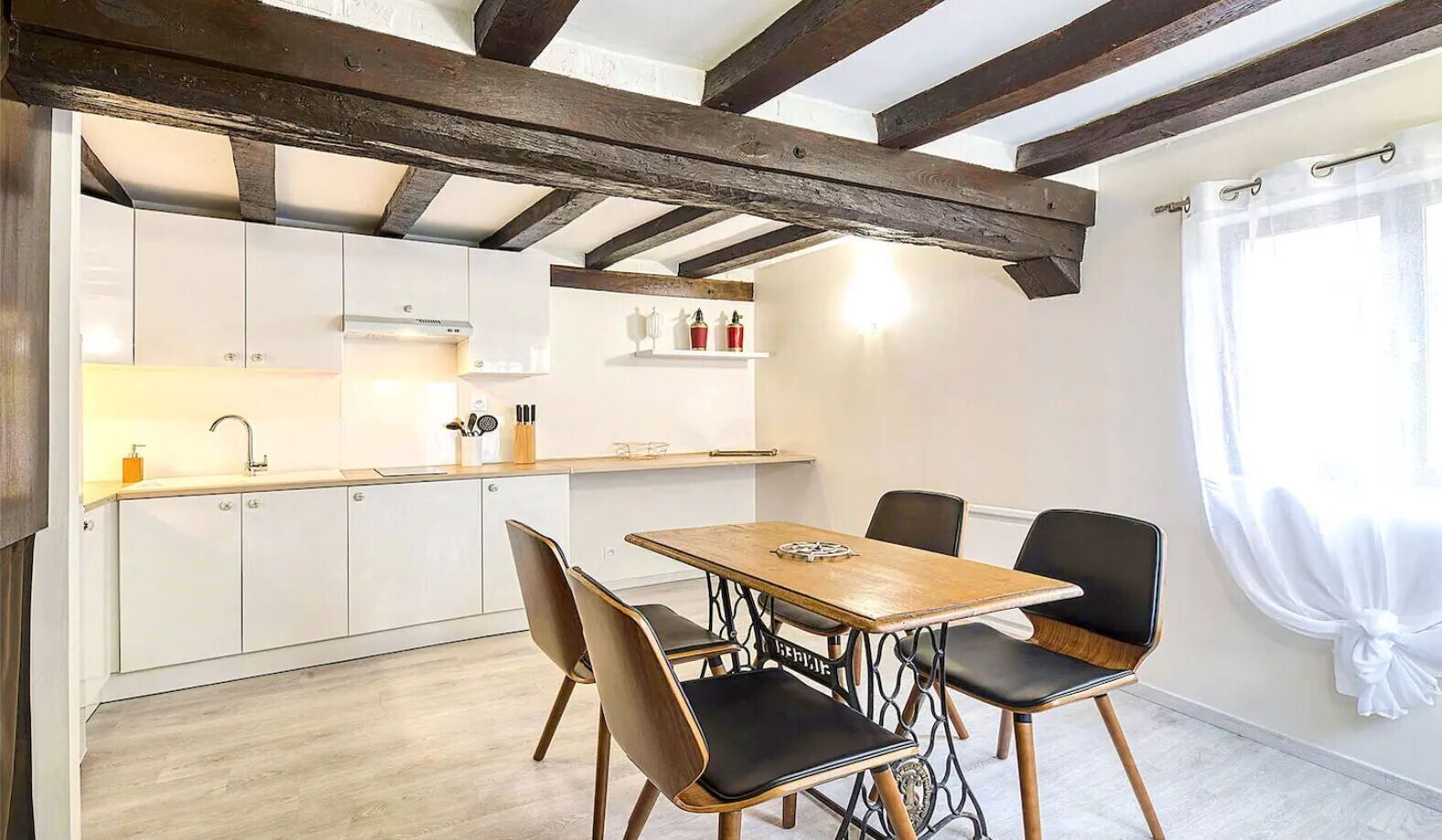 Une cuisine moderne avec des meubles blancs, une table à manger en bois et des chaises noires.