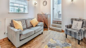 A cozy living room with a grey sofa, a plaid armchair, a wooden cabinet, and a large window. - 1 bedroom accommodation in Chelmorton (Chelmorton)