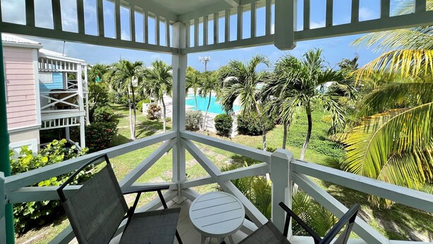 A covered outdoor area with a pool, palm trees, and a view of a building with a blue roof. - 5 Minute walk to the beach! (Christiansted)