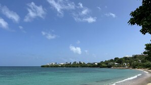 A beach with clear turquoise water, a sandy shore, and buildings on a hillside in the background. - 5 Minute walk to the beach! (Christiansted)