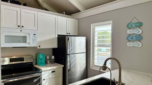 A kitchen with white cabinets, a stainless steel refrigerator, a black oven, a sink with a gold faucet, and a window with a view of greenery. - 5 Minute walk to the beach! (Christiansted)