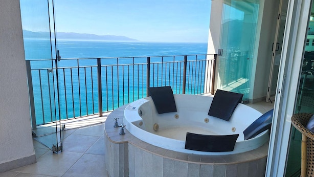 Un balcón con bañera de hidromasaje, puertas de cristal y vista al mar.