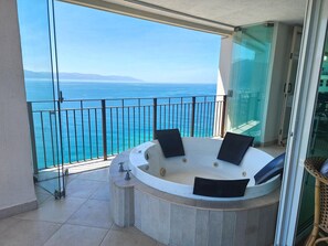 A balcony with a jacuzzi tub, glass doors, and a view of the sea. - Beachfront & stunning views ! (Puerto Vallarta)
