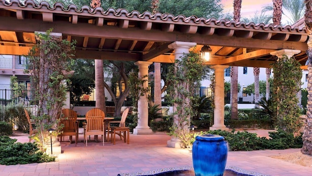 A covered outdoor seating area with a fountain, surrounded by greenery and palm trees. - Mountain Vista C | Studio Legacy Villa (La Quinta)