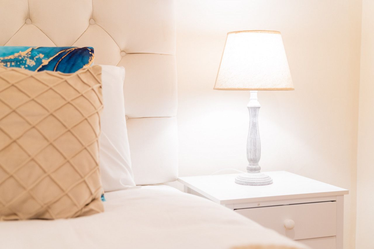 A neatly made bed with a quilted pillow and a white nightstand with a lamp.