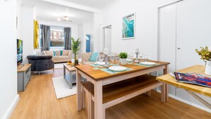 Una sala de estar moderna con una mesa de comedor de madera dispuesta para cuatro personas, un sofá y un televisor.