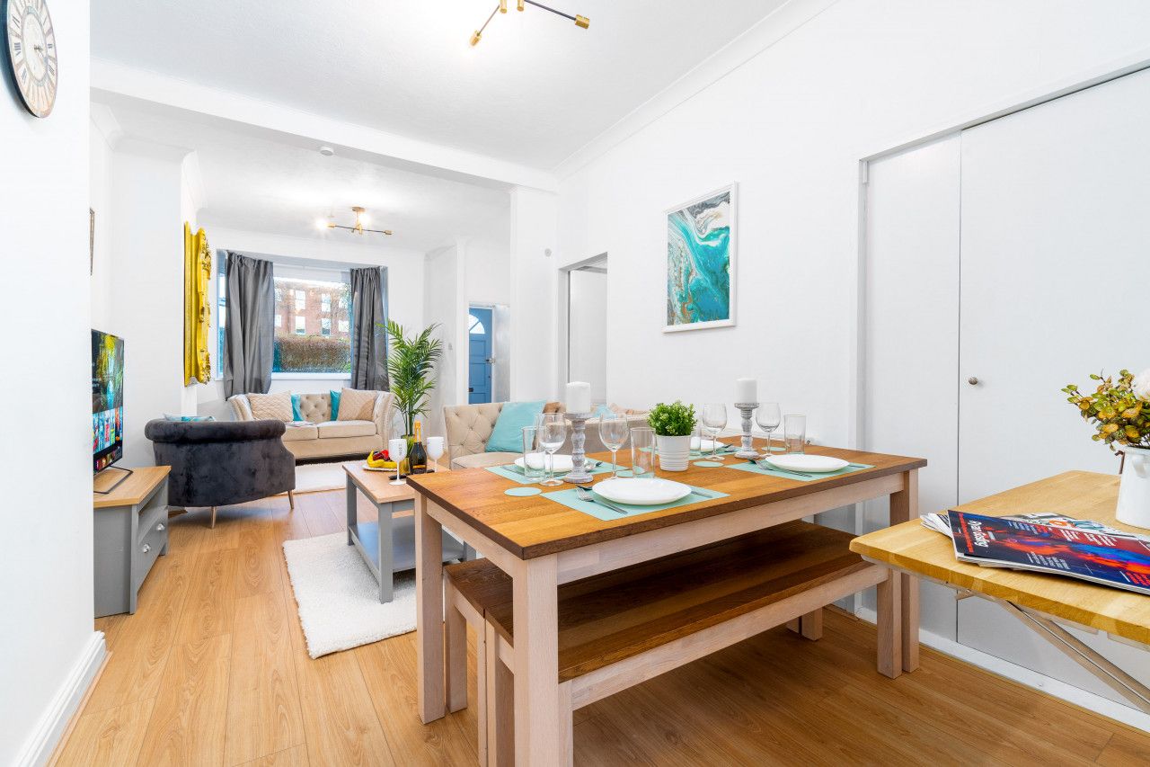 A modern living room with a wooden dining table set for four, a sofa, and a TV.