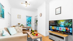 Una sala de estar moderna con sofá, mesa de centro y televisor. Se observa una cocina al fondo, con armarios azules.