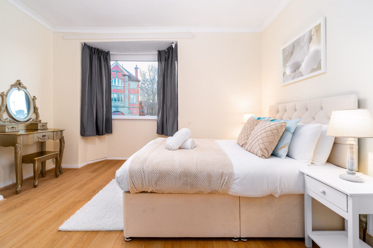 A bedroom with a bed, bedside table, lamp, and a window with curtains.