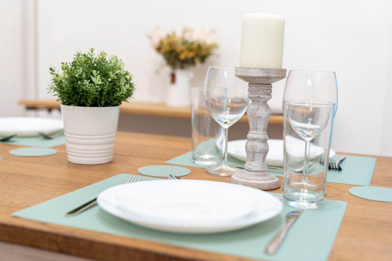 A neatly set dining table with white plates, clear glasses, and a candle holder.