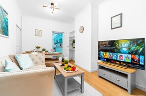 A modern living room with a sofa, coffee table, and TV. There is a kitchen in the background with blue cabinets. - Stylish Three Bedroom House - Harborne - Parking - Garden (Harborne)