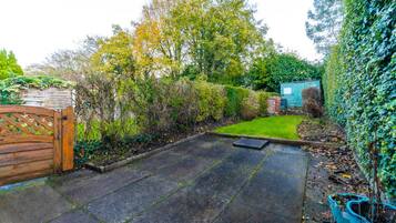 A paved patio area with a wooden gate, a small lawn, and a shed in a garden setting.