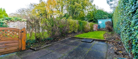 A paved patio area with a wooden gate, a small lawn, and a shed in a garden setting.