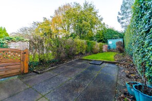 A paved patio area with a wooden gate, a small lawn, and a shed in a garden setting.
