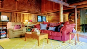 Un interior acogedor de cabaña de madera con un sofá rojo, un sillón color beige y una mesa de centro de madera.