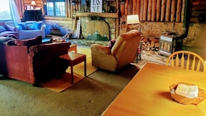 Interior acogedor de una cabaña con chimenea, paredes de madera, un sofá y una mesa de comedor.
