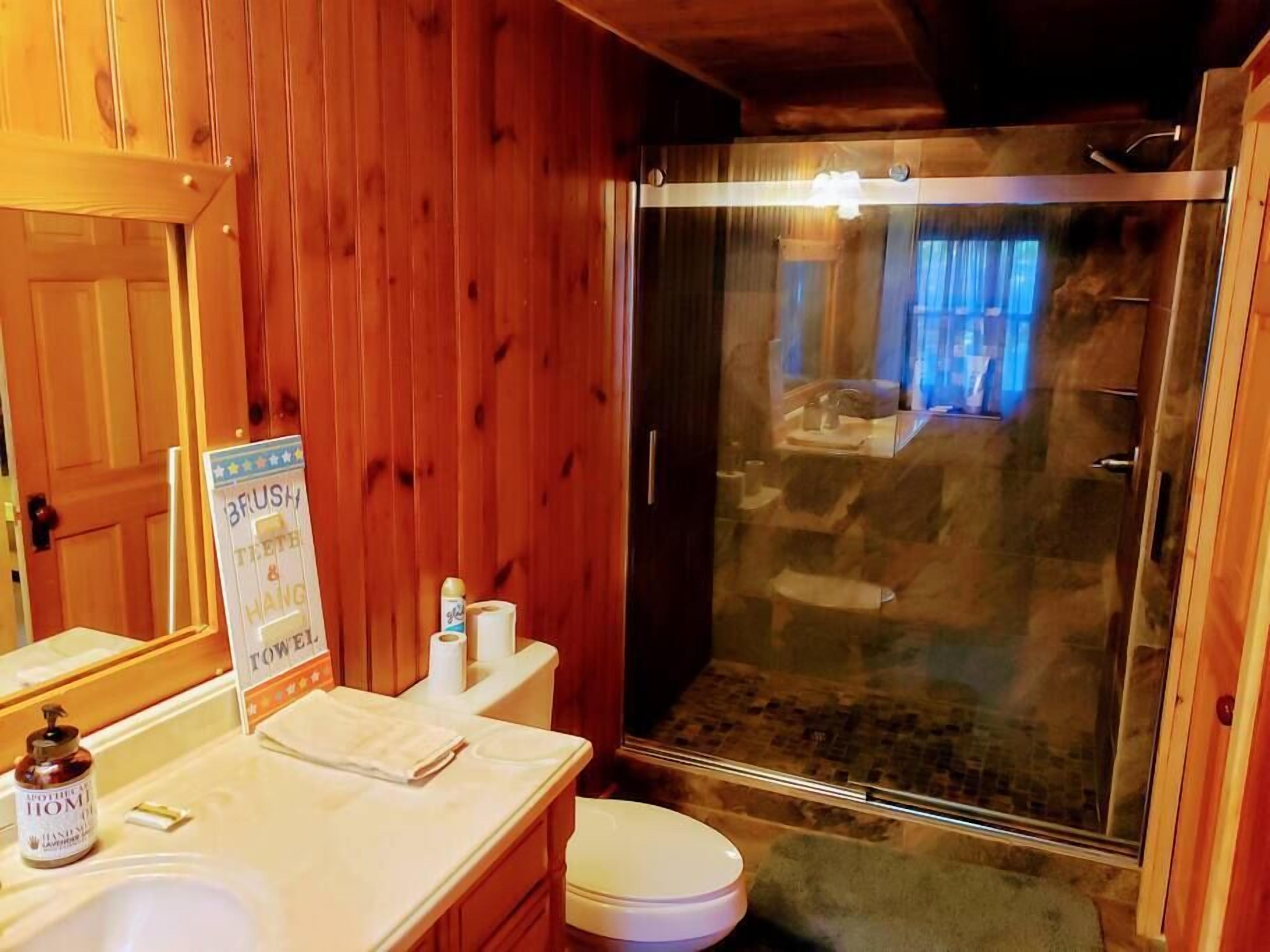 Baño con detalles de madera que incluye ducha, inodoro y lavamanos.