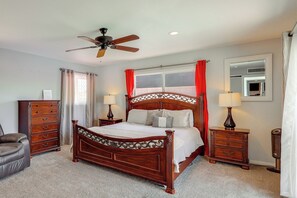 Ein Schlafzimmer mit einem hölzernen Himmelbett, zwei Nachttischen, einem Sessel, einem Deckenventilator und einem Fenster mit Vorhängen.