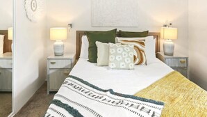 Un dormitorio ordenado con una cama, dos mesitas de noche y un aire acondicionado de pared.