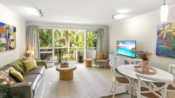 Una sala de estar moderna con sofá, mesa de centro, televisor y zona de comedor.