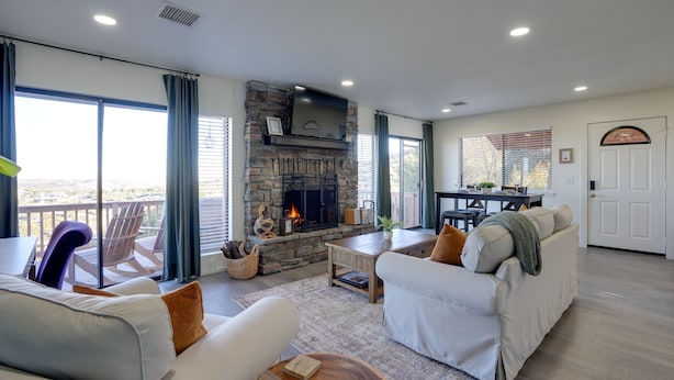 A spacious living room with a stone fireplace, large windows, and a balcony.
