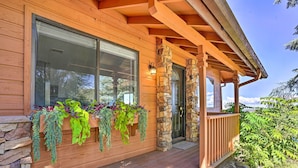 A wooden cabin with a stone foundation, large windows, and a wooden porch with hanging planters.