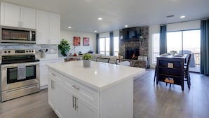 A modern kitchen with white cabinetry, a large island, and a stone fireplace.