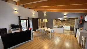 Un salón amplio con mesa de comedor, televisor y cocina al fondo.