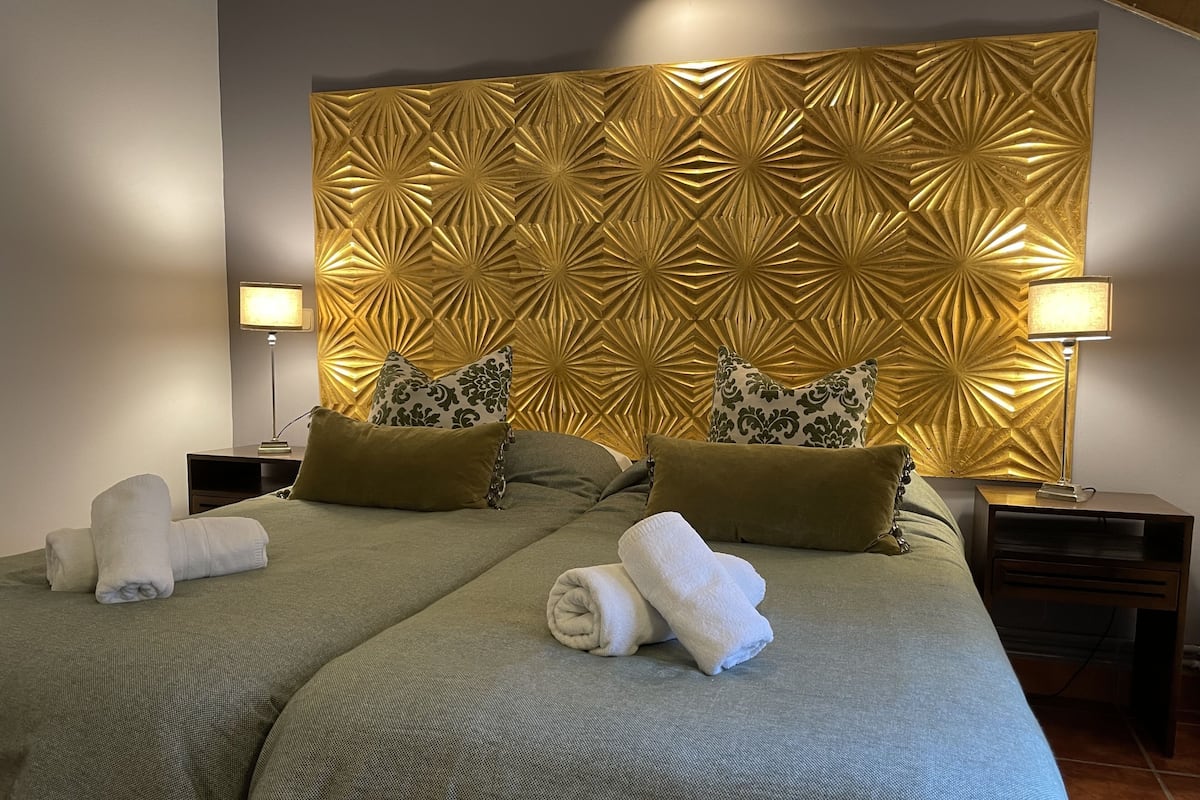 Hotellihuone, jossa on suuri sänky, kaksi yöpöytää ja koristeellinen sängynpääty.
