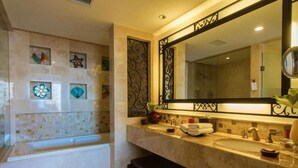 A bathroom with a bathtub, two sinks, a large mirror, decorative tiles, and a wall-mounted vanity.